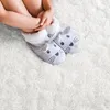 Beine und Füße eines Kindes in grauen Hasen-Hausschuhen mit weißen flauschigen Stulpen, sitzend auf einem weißen zotteligen Teppich Náhled obrázku produktu
