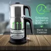 A silver and black electric tea maker is shown on a wooden table, with steam rising from the top. Green arrows indicate heating in the lower chamber, and text overlays highlight fast cooking and warm-up functions. Produktbild-Vorschau