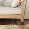 Close-up view of the bottom of a sofa, showing its wooden legs and furniture risers on a wooden floor. Produktbild-Vorschau