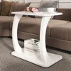 A white C-shaped side table with books on its lower shelf is placed next to a brown sectional sofa in a living room. Anteprima dell’immagine prodotto