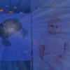 A baby is lying in a crib with a projector creating an underwater scene with fish. Náhled obrázku produktu