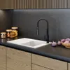 A modern kitchen sink area with a white sink, black faucet, and wooden cabinets. Jars of food and purple onions are on the countertop. Podgląd zdjęcia produktu
