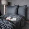 A neatly made bed with a dark gray checkered duvet cover and two pillows, featuring an open book and glasses. Náhled obrázku produktu