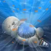 A plush toy otter lying on its back underwater, projecting stars and fish. Produktbild-Vorschau