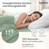 A woman sleeping peacefully on a bed with green bedding. Produktbild-Vorschau