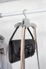 A gray handbag hanger with two straps of a handbag hanging from it, attached to a closet rod. Produktbild-Vorschau