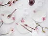 A table setting with floral-decorated plates and cutlery, alongside glasses and magnolia branches. Náhľad obrázku produktu