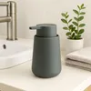 A gray ceramic soap dispenser sits on a bathroom counter next to a sink and a small potted plant. Podgląd zdjęcia produktu