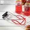 A jar lifter tool is shown next to jars filled with red liquid, with apples in the background. Anteprima dell’immagine prodotto