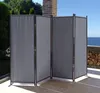 A gray, four-panel folding screen is set up on a patio with a view of the ocean and trees. Produktbild-Vorschau