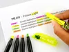 A hand is holding a yellow highlighter over a piece of paper with text and colored swatches. Náhled obrázku produktu
