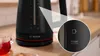A close-up view of a black Bosch electric kettle with red accents, showing the water level indicator and a magnified view of the maximum fill line. Podgląd zdjęcia produktu