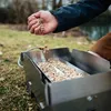A person is adding wood chips to a smoking tray outdoors. Produktbild-Vorschau