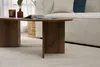 A close-up view of a wooden coffee table in a living room setting, with a sofa in the background. Produktbild-Vorschau