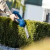 A person is using a cordless hedge trimmer to trim a bush. Produktbild-Vorschau