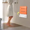 A person is standing in a shower stall next to a wall-mounted folding shower seat. Náhled obrázku produktu