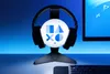 A PlayStation headset stand with a glowing orb featuring PlayStation symbols, placed on a desk with a keyboard and monitor in the background. Anteprima dell’immagine prodotto