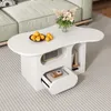 A white, cloud-shaped coffee table with storage compartments, placed on a light gray carpet in a living room setting. Produktbild-Vorschau