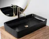 A black rectangular vessel sink with gold accents and a gold faucet, placed on a wooden surface. Produktbild-Vorschau