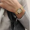 A close-up shot of a person's wrist wearing a gold watch and a bracelet, with a black bag visible. Produktbild-Vorschau