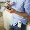 A man in a blue shirt and jeans is holding a smartphone and glasses, with a baby monitor clipped to his jeans pocket. Produktbild-Vorschau
