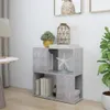A small, two-tiered bookshelf with a concrete-like finish, placed in a room setting with a lamp and a plant.