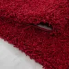 A close-up view of a red shaggy rug, showing its texture and the underside where it is folded. Produktbild-Vorschau