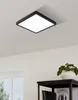 A square LED ceiling light is mounted on a white ceiling. Below the light, a dark shelf holds a white pot with a green plant. Produktbild-Vorschau