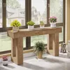 A wooden console table with plants placed on and around it, in front of a large window with a view of houses. Náhľad obrázku produktu