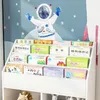 A white bookshelf filled with children's books, with an astronaut illustration on the wall behind it. Náhled obrázku produktu