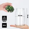 A hand holds a lid with a cucumber pattern over an empty glass jar, with measurement indicators and weight information displayed next to it. Podgląd zdjęcia produktu