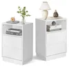 Two white bedside tables are shown side-by-side against a white background. The table on the left has a book, a clock, and a vase with greenery on top, and two drawers below. The table on the right has a lamp, a vase, and books on top, and two drawers belo Náhled obrázku produktu