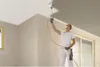 A person is painting a ceiling with a spray gun in a room under renovation. Produktbild-Vorschau