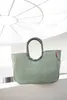A sage green tote bag with a gray handle is placed on a white ledge, with a white ceiling structure in the background. Voir les images du produit