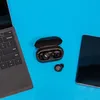A pair of black wireless earbuds in their charging case, a single earbud, a smartphone, and a laptop are arranged on a blue background. Produktbild-Vorschau