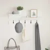 A white wall with a white shelf and coat rack, decorated with a plant, a picture frame, a cap, a bag, and a scarf. Voir les images du produit