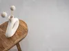 A white vase with decorative spheres on sticks sits on a wooden stool against a textured gray background. Produktbild-Vorschau