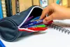A hand is reaching into a pencil case to take out a blue pen. Voir les images du produit