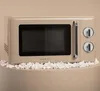 A retro-style beige microwave oven is displayed on a surface covered with popcorn. Produktbild-Vorschau