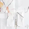 A close-up view of a fabric with a printed pattern of branches and leaves, overlaid on text from a book or magazine. Produktbild-Vorschau