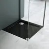 A close-up view of a modern black shower tray with a chrome drain, set against a dark gray wall and a light gray tiled floor.