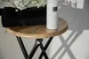 A white bottle of toiletries sits on a wooden stool next to black towels and white flowers. Produktbild-Vorschau