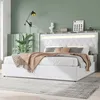 A bedroom scene with a white bed as the main focus, decorated with pillows and a throw blanket. The wall behind the bed is painted green, and there's a wall lamp and some decorative items on a shelf above the headboard. Náhľad obrázku produktu