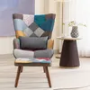 A patchwork armchair with a small cushion is placed on a rug in a room, next to a side table with a vase and a cup. Náhled obrázku produktu