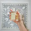 A hand holding a perfume bottle in front of a decorative wall panel. Anteprima dell’immagine prodotto