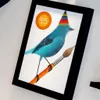A framed picture of a blue bird wearing a party hat and holding a paintbrush. Produktbild-Vorschau