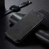 A black leather flip-style phone case is displayed diagonally on a dark, textured surface, with a black smartwatch in the background. Produktbild-Vorschau