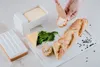 A hand is spreading butter on a slice of bread from a butter dish. Podgląd zdjęcia produktu