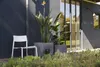 A modern outdoor patio scene with a white chair, two large planters with plants, and a glass door. Produktbild-Vorschau