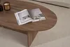 A close-up of an oval coffee table with an open magazine and a candle on it, placed on a textured rug. Anteprima dell’immagine prodotto